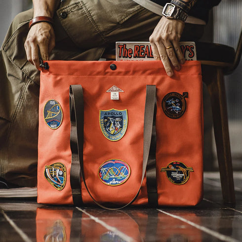 Person holding an orange tote bag with patches on a reflective surface
